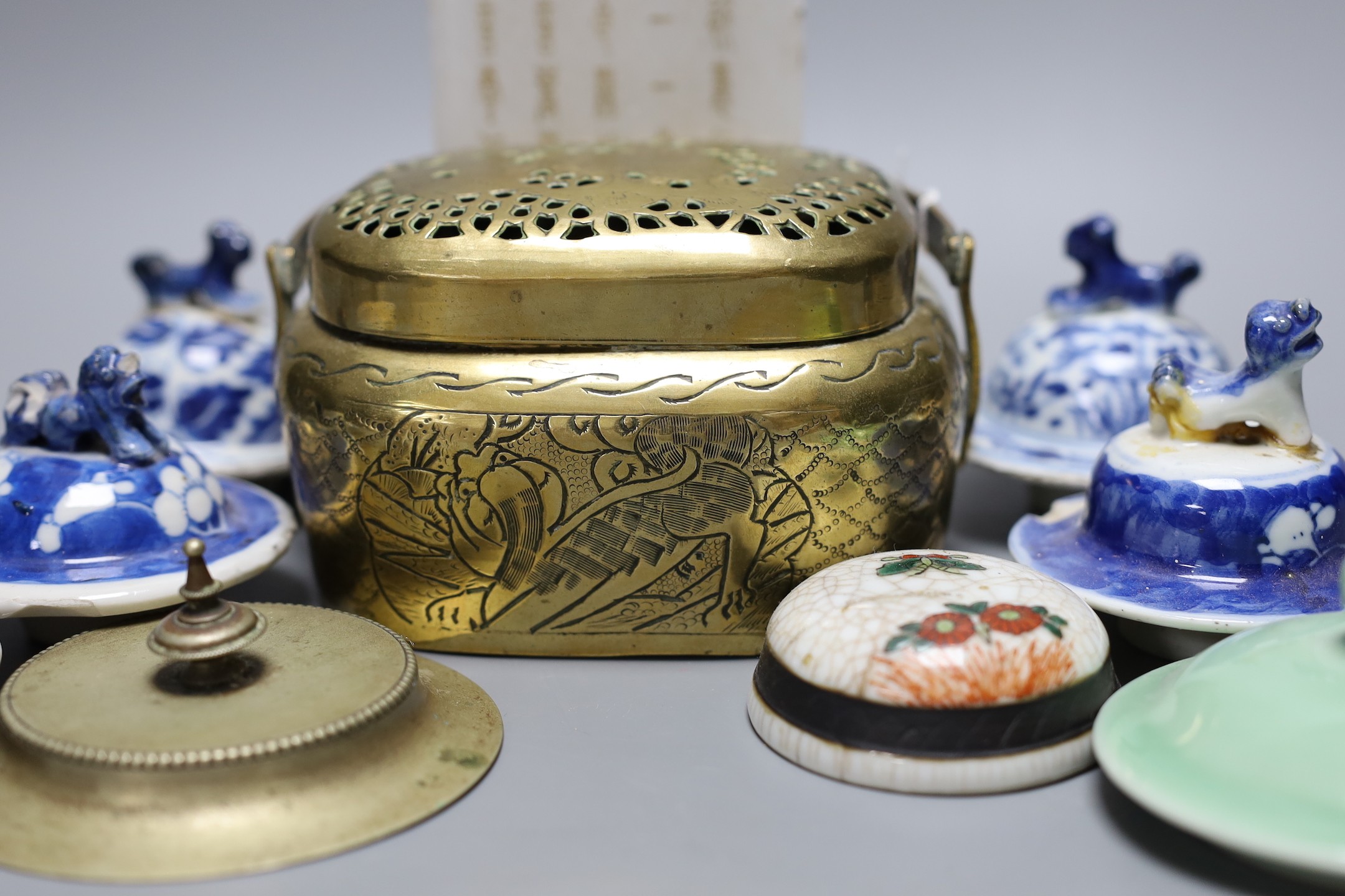 A collection of various Chinese porcelain lids/covers, a clobbered blue and white tea bowl, a brass hand warmer and a hardstone tablet